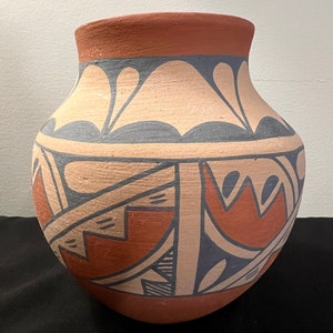 May include: A hand-painted pottery jar with a geometric design in shades of brown, white, and blue. The jar has a rounded body and a wide opening.