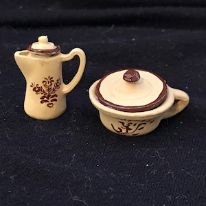 May include: A set of two miniature ceramic kitchenware pieces. A brown and white creamer with a floral design and a brown and white covered dish with a floral design.