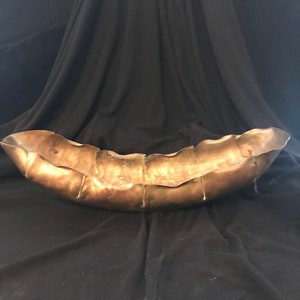 May include: A large, gold-colored metal bowl with a wavy, organic shape. The bowl is made of hammered metal and has a rustic, handmade look.