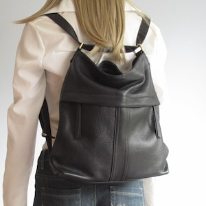 Peut inclure: Un sac à dos en cuir noir avec une silhouette souple et affaissée, présentant une couture horizontale sur la partie supérieure, deux lignes verticales cousues sur le panneau avant et des bretelles réglables fixées par des boucles métalliques.