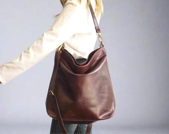 May include: A large, burgundy leather shoulder bag with a long strap and gold-colored hardware. The bag has a slouchy design and is worn over the shoulder. The bag is made of a smooth, shiny leather.