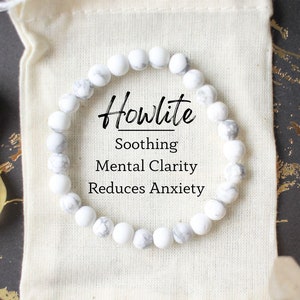 May include: White howlite beaded bracelet in a white drawstring bag. The bag has the text "Howlite" with the words "Soothing", "Mental Clarity", and "Reduces Anxiety" printed below.