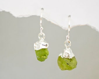 May include: A pair of silver earrings with green gemstone drops. The gemstones are rough and have a natural, unpolished look.