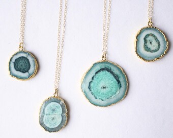 May include: Four gold necklaces with different sized round agate pendants. The agate is a light blue and green color with a white center.