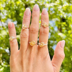 May include: A hand wearing five rings with small, clear, yellow-toned stones set in silver wire.