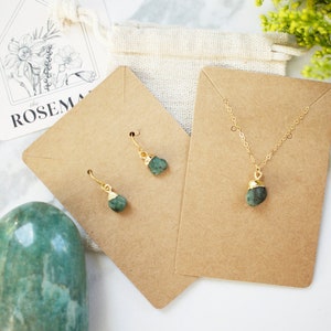 May include: A set of green gemstone jewelry featuring a necklace and earrings. The necklace and earrings have gold accents and are displayed on brown card stock.