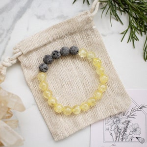 Könnte beinhalten: Ein gelbes und schwarzes Perlenarmband mit Lavasteinen. Das Armband befindet sich in einem kleinen, weißen Beutel.