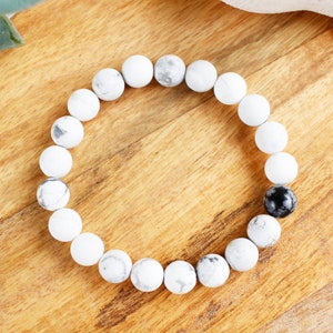 May include: White and black beaded bracelet with a single black bead. The bracelet is made of round, smooth beads.
