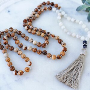 Pode incluir: Um colar mala de pedras preciosas marrons e brancas com um tassel. O colar &eacute; feito de contas redondas e tem uma conta cinza escura no final.