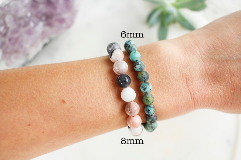 May include: Two beaded bracelets on a wrist. The bracelet on the left is made of 8mm beads in shades of pink, white, and black. The bracelet on the right is made of 6mm turquoise beads.