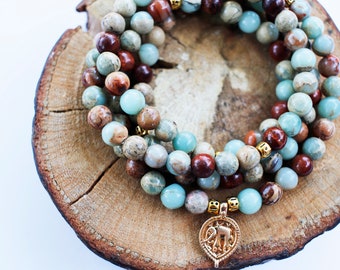 Puede incluir: Un conjunto de tres pulseras de cuentas con un dije de elefante de oro. Las pulseras están hechas de piedras marrones, verdes y azules.