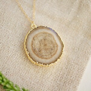May include: A gold chain necklace with a round pendant featuring a brown and white agate slice with a gold rim.