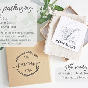 Puede incluir: Una caja de regalo marr&oacute;n con una etiqueta blanca que dice "The Rosemary Room". La caja est&aacute; llena de una bolsa de muselina blanca que contiene una tarjeta blanca con una ilustraci&oacute;n en blanco y negro de romero y el texto "Rosemary".