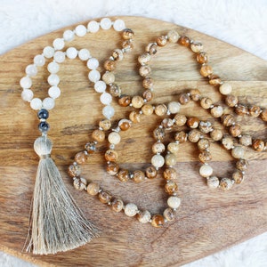 Pode incluir: Um colar mala de pedras preciosas marrons e brancas com um tassel. O colar &eacute; feito de pedras naturais e &eacute; enfiado em um cord&atilde;o. O tassel &eacute; feito de fio marrom e branco.