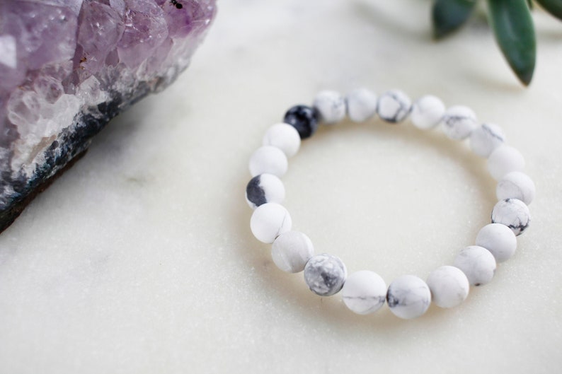 May include: White and black marble beaded bracelet. The bracelet is made of round beads with a white base and black marbling.