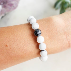 May include: A white and black beaded bracelet with a single black bead in the center.