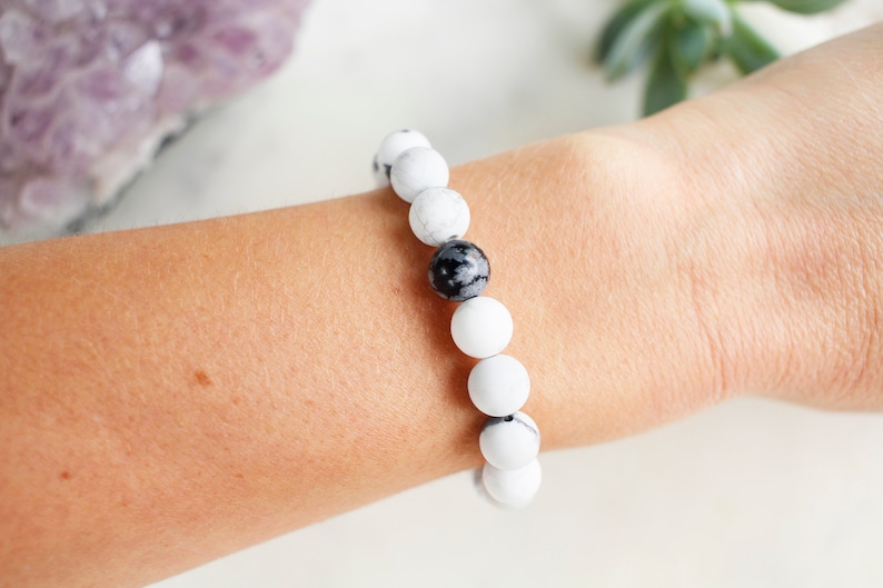 May include: A white and black beaded bracelet with a single black bead in the center.