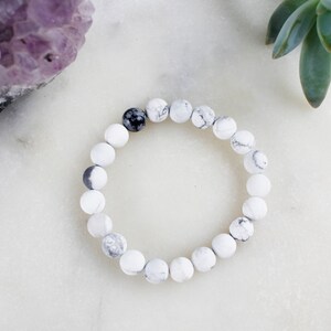 May include: White and black marble bead bracelet with a single black bead.