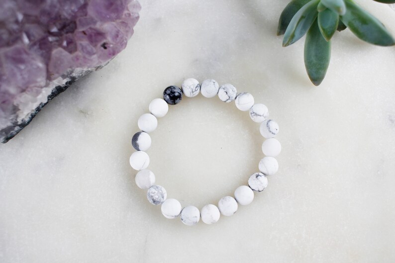 May include: White and black marble bead bracelet with a single black bead.