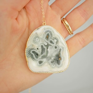 May include: A gold chain necklace with a large, white agate pendant. The agate has a unique, swirling pattern of gray and white.