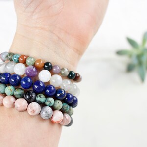 May include: A stack of colorful beaded bracelets on a person's wrist. The bracelets are made of various stones, including turquoise, lapis lazuli, and rose quartz.