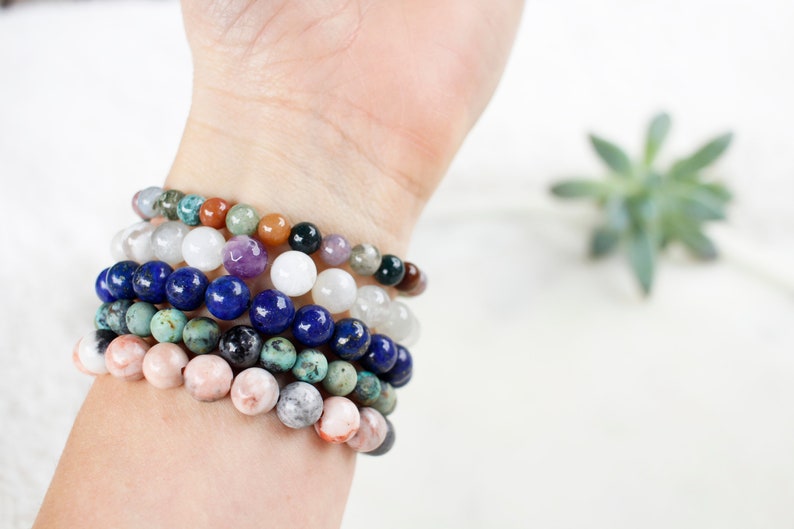May include: A stack of colorful beaded bracelets on a person's wrist. The bracelets are made of various stones, including turquoise, lapis lazuli, and rose quartz.