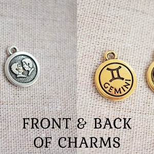 May include: Two Gemini zodiac charms, one silver and one gold, displayed front and back. The front of each charm features the Gemini symbol and the word "GEMINI". The back of each charm shows two figures.