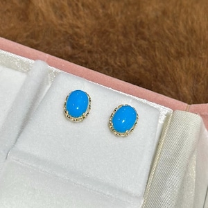May include: A pair of oval-shaped stud earrings featuring bright blue cabochon stones set in a delicate gold-toned metal frame with a twisted rope-like edge detail, presented on a white padded display insert.
