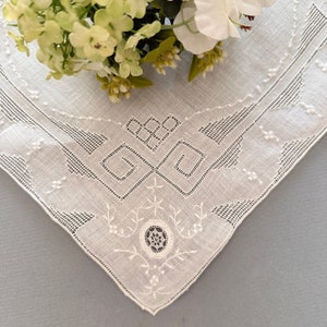 May include: A white linen handkerchief with delicate white embroidery in a geometric pattern. The handkerchief has a scalloped edge.