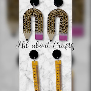 May include: A pair of earrings featuring a black circle stud, with a pencil-shaped design in leopard print and pink accents, and a ruler-shaped design in yellow with black markings. The text "Ahl about Crafts" is visible.