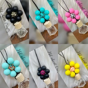 May include: A collection of car air fresheners with flower-shaped designs. Each freshener features a cluster of colorful beads and a decorative center bead, attached to a small glass bottle with a wooden cap. The text "Ahl about Crafts" is visible.