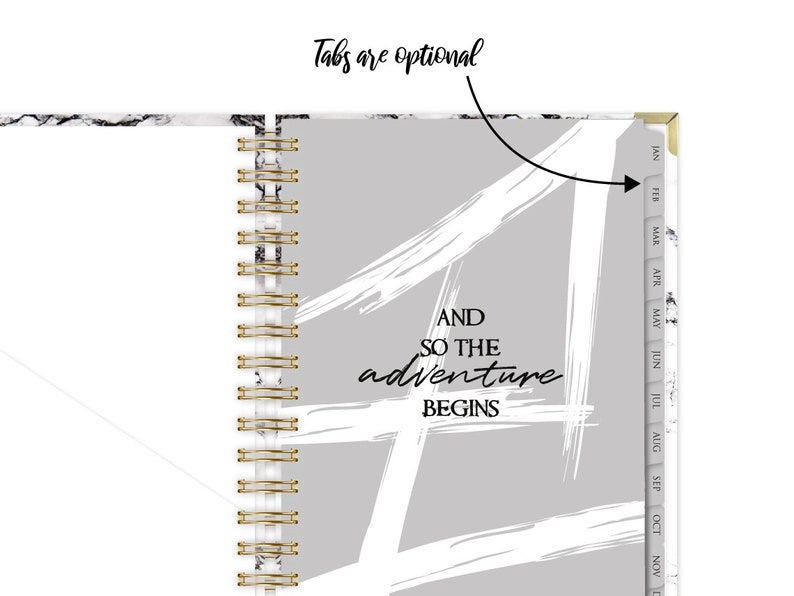 Może przedstawiać: Szary i biały planer z marmurową okładką i złotym spiralnym oprawieniem. Okładka ma biały wz&oacute;r z pociągnięć pędzlem i tekst "AND SO THE adventure BEGINS". Planer ma zakładki na każdy miesiąc roku.