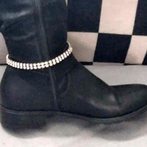 May include: Black leather boot with a double-strand rhinestone anklet. The anklet is made of small, clear rhinestones set in a silver-tone metal. The boot has a low heel and a smooth, matte finish.
