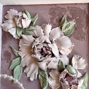 May include: A framed artwork featuring a 3D textured painting of white peonies with green leaves on a light brown background.