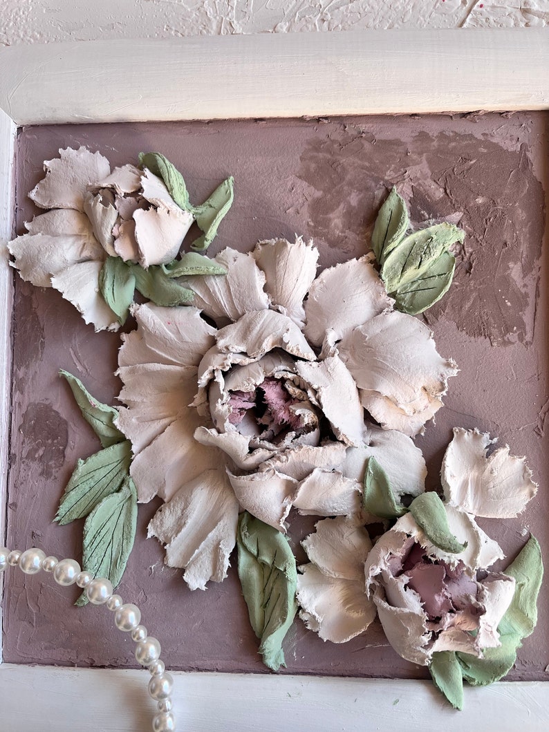 May include: A framed artwork featuring a 3D textured painting of white peonies with green leaves on a light brown background.