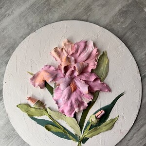 K&ouml;nnte beinhalten: Eine runde, wei&szlig;e Leinwand mit einer dreidimensionalen rosa und orangefarbenen Iris-Blume mit gr&uuml;nen Bl&auml;ttern. Die Blume ist realistisch gemalt und hat eine strukturierte Oberfl&auml;che.