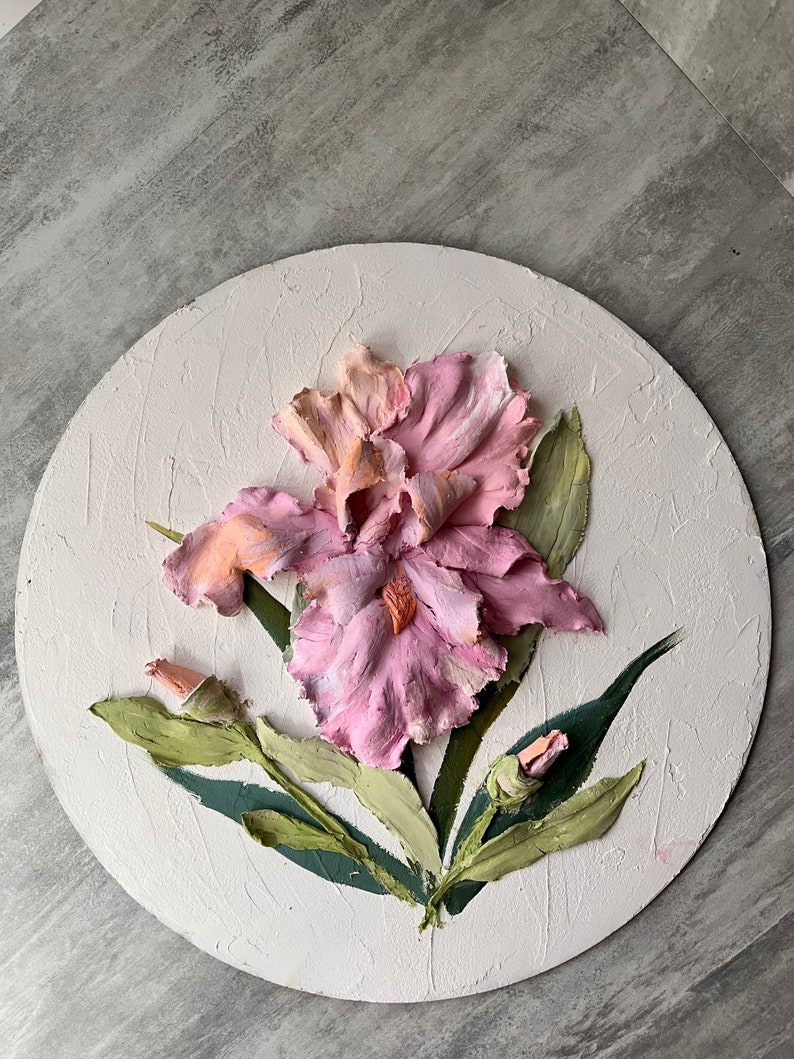 K&ouml;nnte beinhalten: Eine runde, wei&szlig;e Leinwand mit einer dreidimensionalen rosa und orangefarbenen Iris-Blume mit gr&uuml;nen Bl&auml;ttern. Die Blume ist realistisch gemalt und hat eine strukturierte Oberfl&auml;che.
