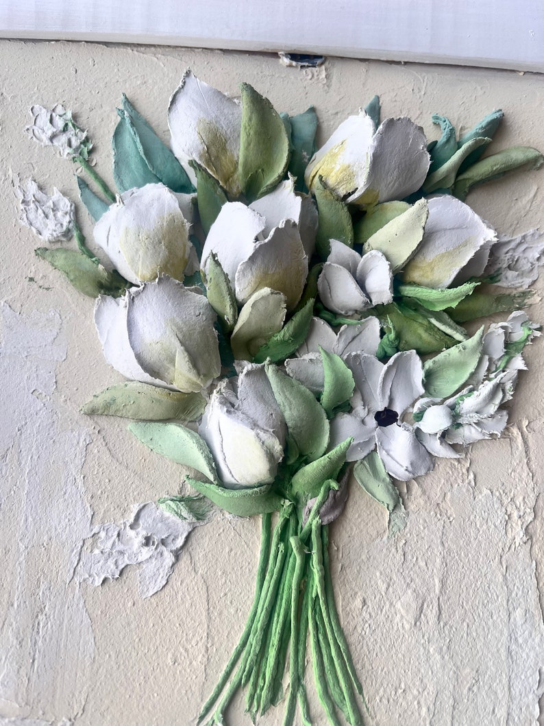 May include: A white and green 3D floral painting with a textured surface. The painting features a bouquet of white flowers with green leaves and stems.
