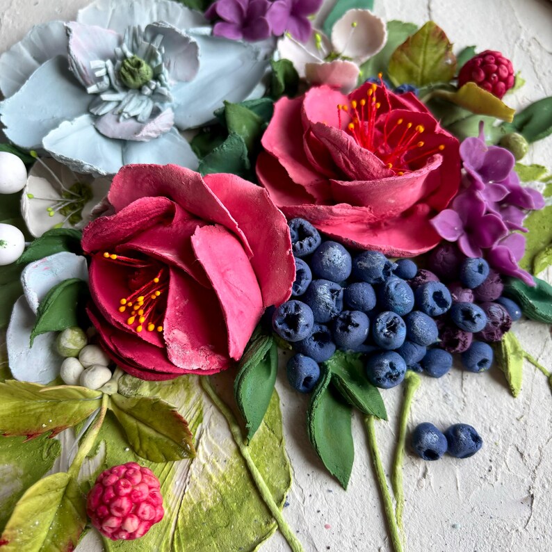 May include: A close-up of a textured artwork depicting a floral arrangement. It features large, pink roses, blueberries, and purple and white flowers. Green leaves and stems are set against a textured background, creating a vibrant contrast.