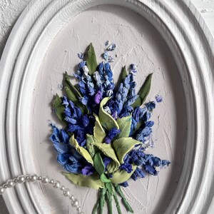 May include: A framed painting of a bouquet of blue and green flowers. The flowers are made of fabric and are arranged in a realistic style. The painting is set against a white background.