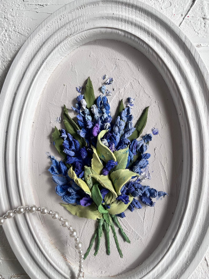 May include: A framed painting of a bouquet of blue and green flowers. The flowers are made of fabric and are arranged in a realistic style. The painting is set against a white background.