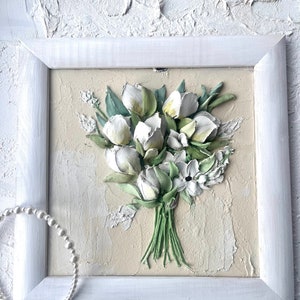 May include: A white framed painting of a bouquet of white flowers with green leaves on a beige background.