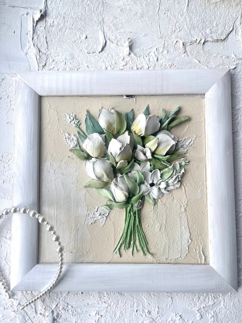 May include: A white framed painting of a bouquet of white flowers with green leaves on a beige background.