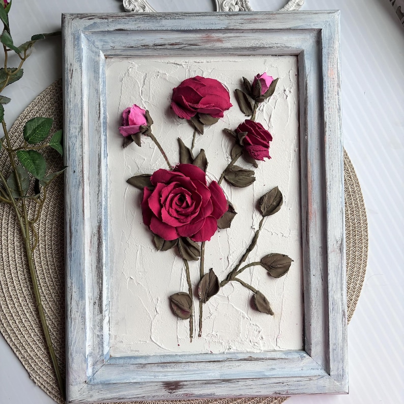 May include: A framed painting of a floral arrangement with pink and red roses on a textured white background. The frame is a light blue color with a distressed finish.