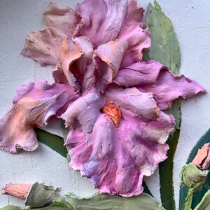 K&ouml;nnte beinhalten: Nahaufnahme einer rosa und wei&szlig;en Iris-Blume, die aus Ton geformt wurde. Die Blume bl&uuml;ht und hat eine zarte, strukturierte Oberfl&auml;che. Der Hintergrund ist eine wei&szlig;e Wand.