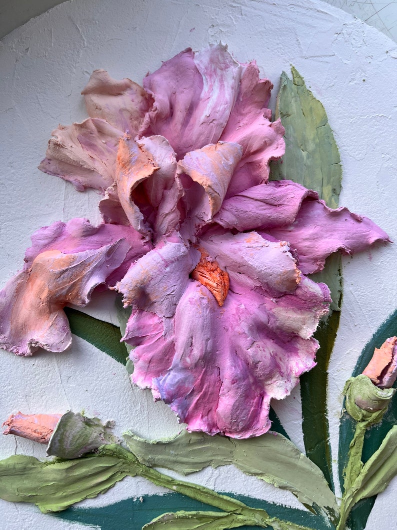 K&ouml;nnte beinhalten: Nahaufnahme einer rosa und wei&szlig;en Iris-Blume, die aus Ton geformt wurde. Die Blume bl&uuml;ht und hat eine zarte, strukturierte Oberfl&auml;che. Der Hintergrund ist eine wei&szlig;e Wand.