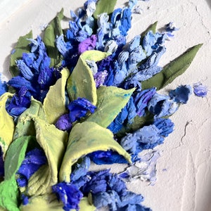 May include: A close-up of a 3D painting of blue and green flowers. The flowers are painted in a realistic style and have a textured surface.