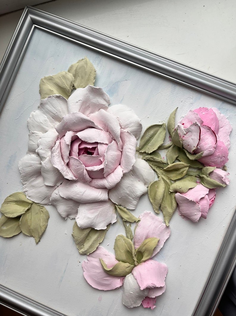 Peut inclure: Une &oelig;uvre d'art murale 3D encadr&eacute;e repr&eacute;sentant un groupe de roses roses et blanches avec des feuilles vertes. Les roses sont sculpt&eacute;es et peintes pour para&icirc;tre r&eacute;alistes.
