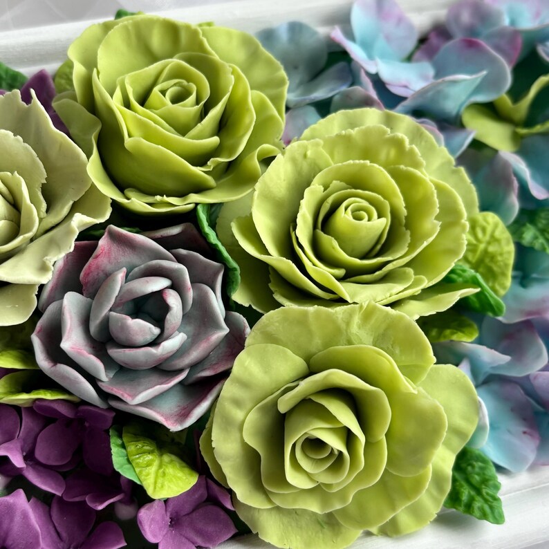 May include: Close-up of a floral arrangement featuring vibrant green roses, purple and blue hydrangeas, and a succulent with pink edges. The flowers are arranged closely together, creating a dense and colorful display. The overall aesthetic is fresh and natural.