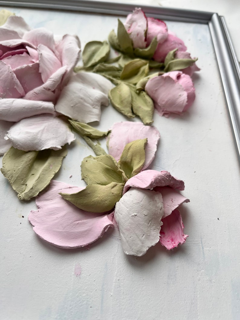 Peut inclure: Une &oelig;uvre d'art murale 3D encadr&eacute;e repr&eacute;sentant un groupe de roses roses et blanches avec des feuilles vertes. Les roses sont sculpt&eacute;es et ont un aspect textur&eacute;.
